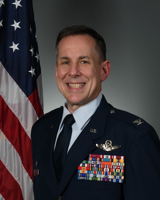 Air Force colonel stands in front of American flag.