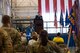 A crowd of Airmen and local civic leaders watch as Colonel Scott Hurrelbrink, in his full service dress, speaks at a on-stage podium in the distance