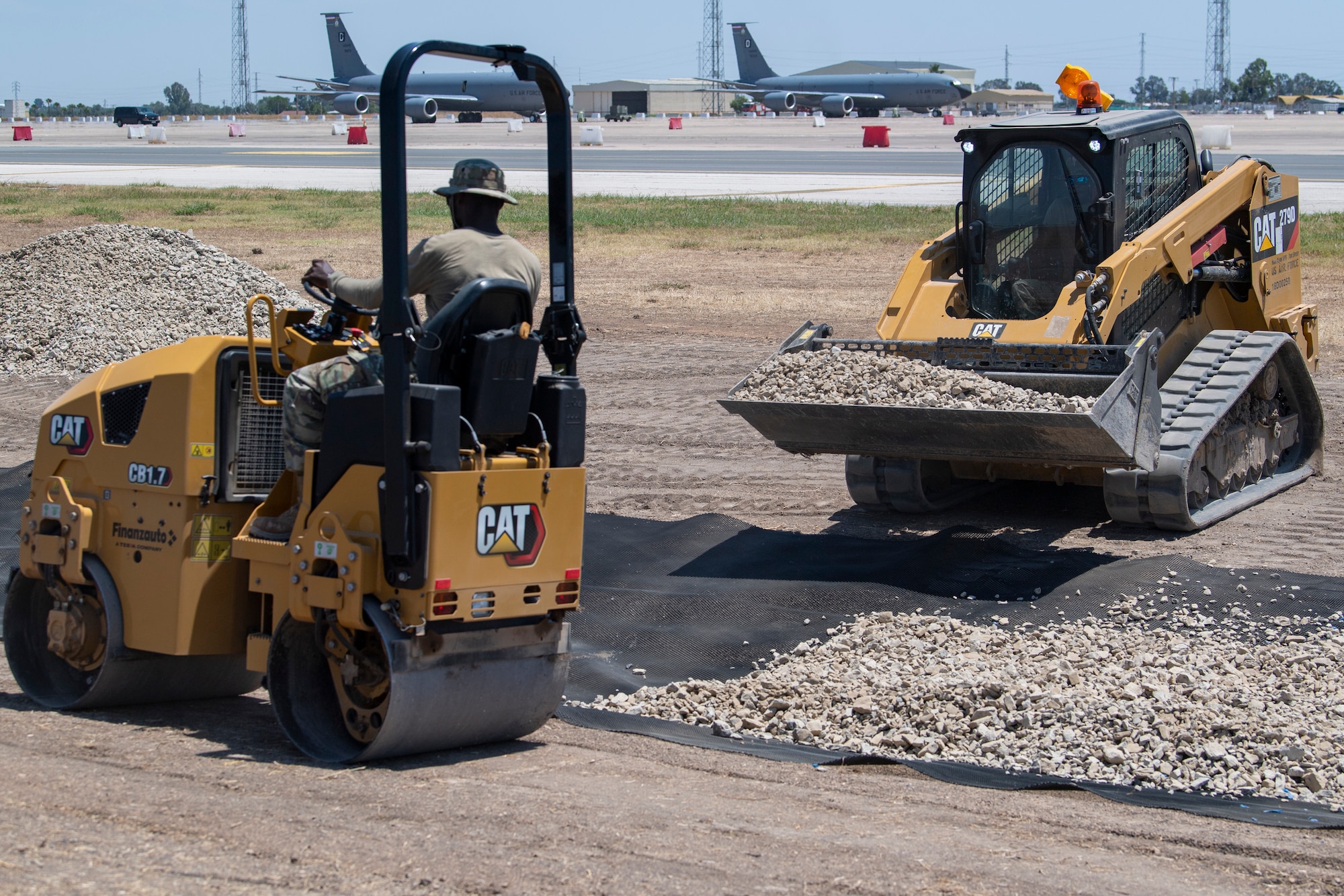U.S. Air Force Amn. Legre Gnahoua, a heavy equipment and pavements operator with the 514th Civil Engineer Squadron, 514th Air Mobility Wing, uses a vibratory roller to level the ground while Sr. Amn. Olumoroti Coker, a heavy equipment and pavements operator with the 514th CES, 514th AMW, dumps gravel into a ditch using a skid steer loader to prevent erosion at the airfield on Morón Air Base, Spain, June 24, 2024.