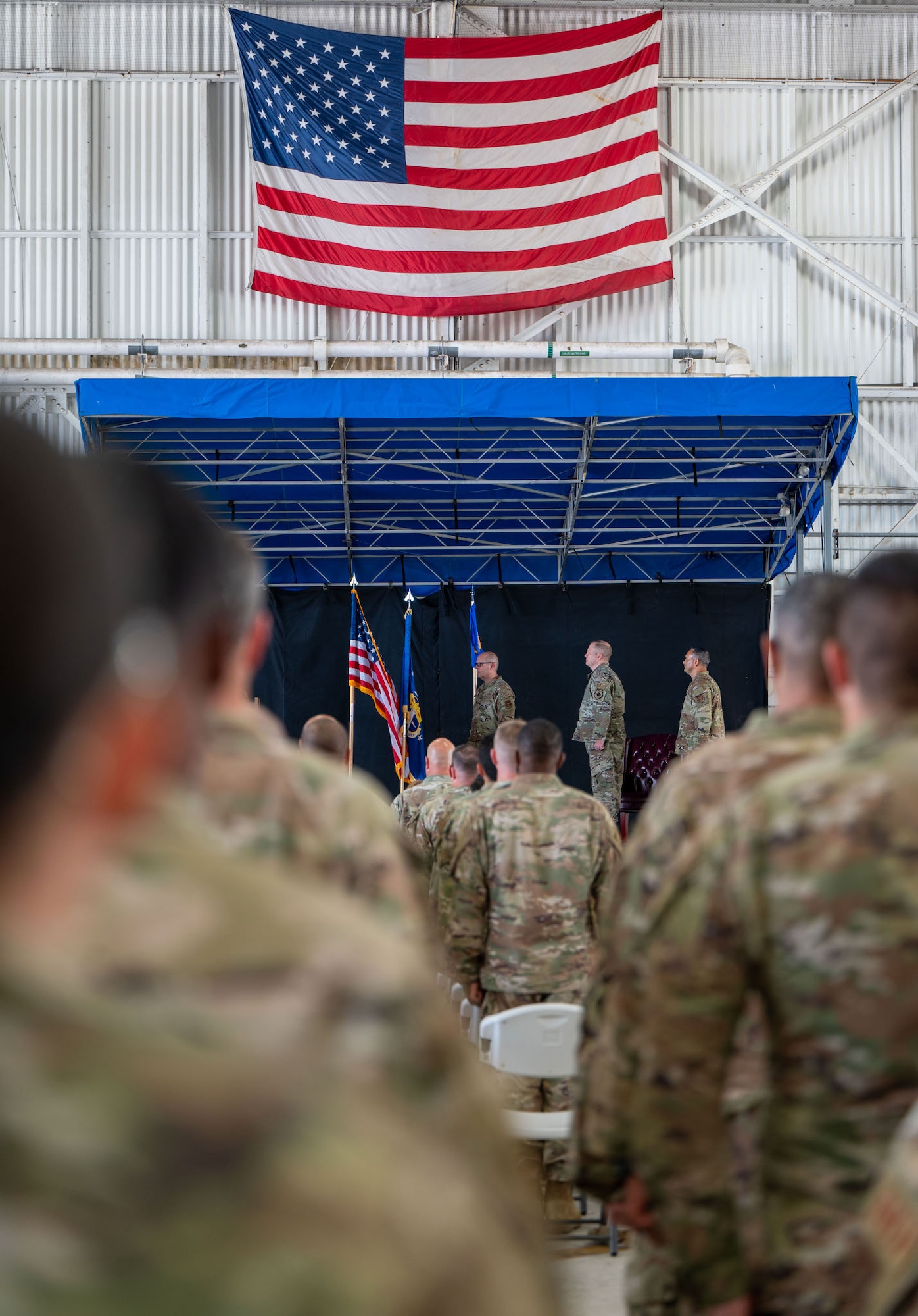 Col. Jessie Hamilton, center, 920th Rescue Wing commander, and Col. Anthony Colberg, right, incoming 920th Maintenance Group commander, along with members of the audience stand at attention.