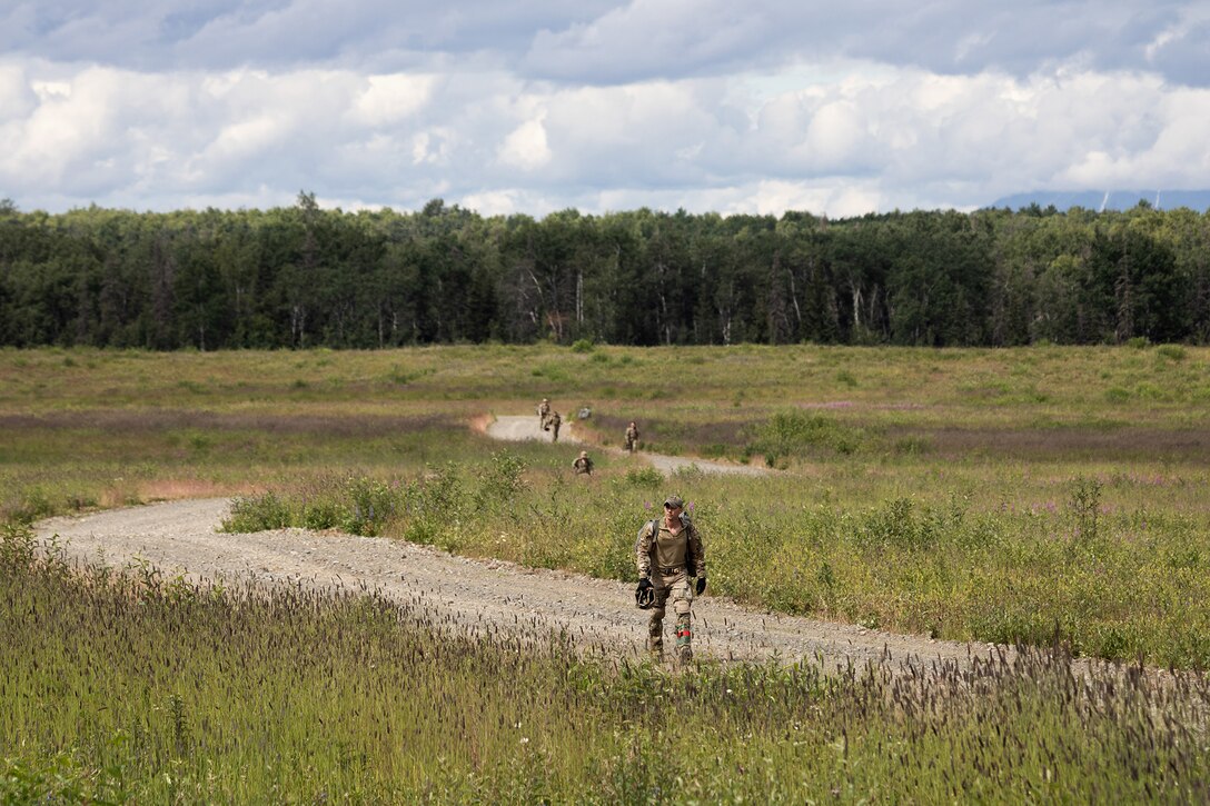 Airmen walk down a dirt trail through a grassy area during daylight.