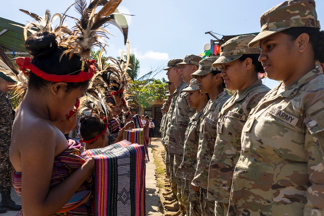 Timor-Leste students in ceremonial dress present scarf-like gifts to soldiers standing in a row.