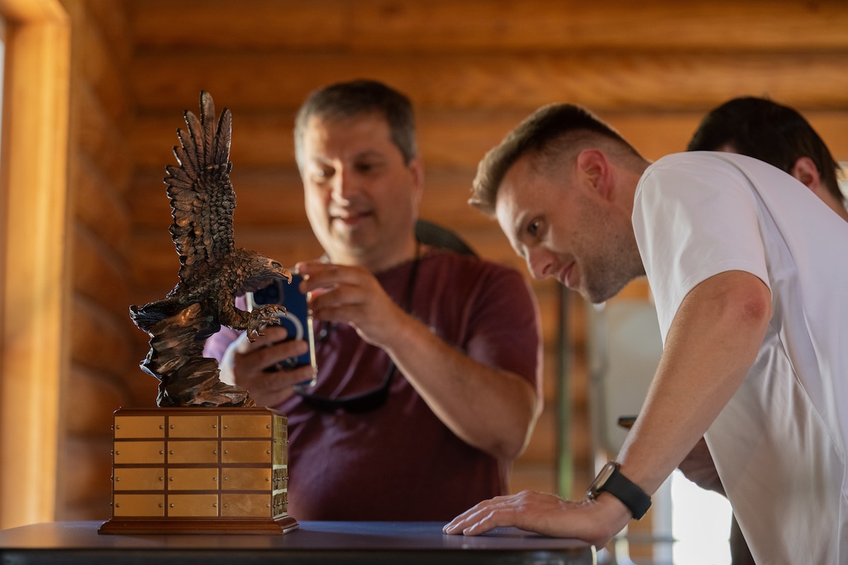 Individuals take photos and look at the 2024 Young Guns vs. Old Pistols Challenge trophy.