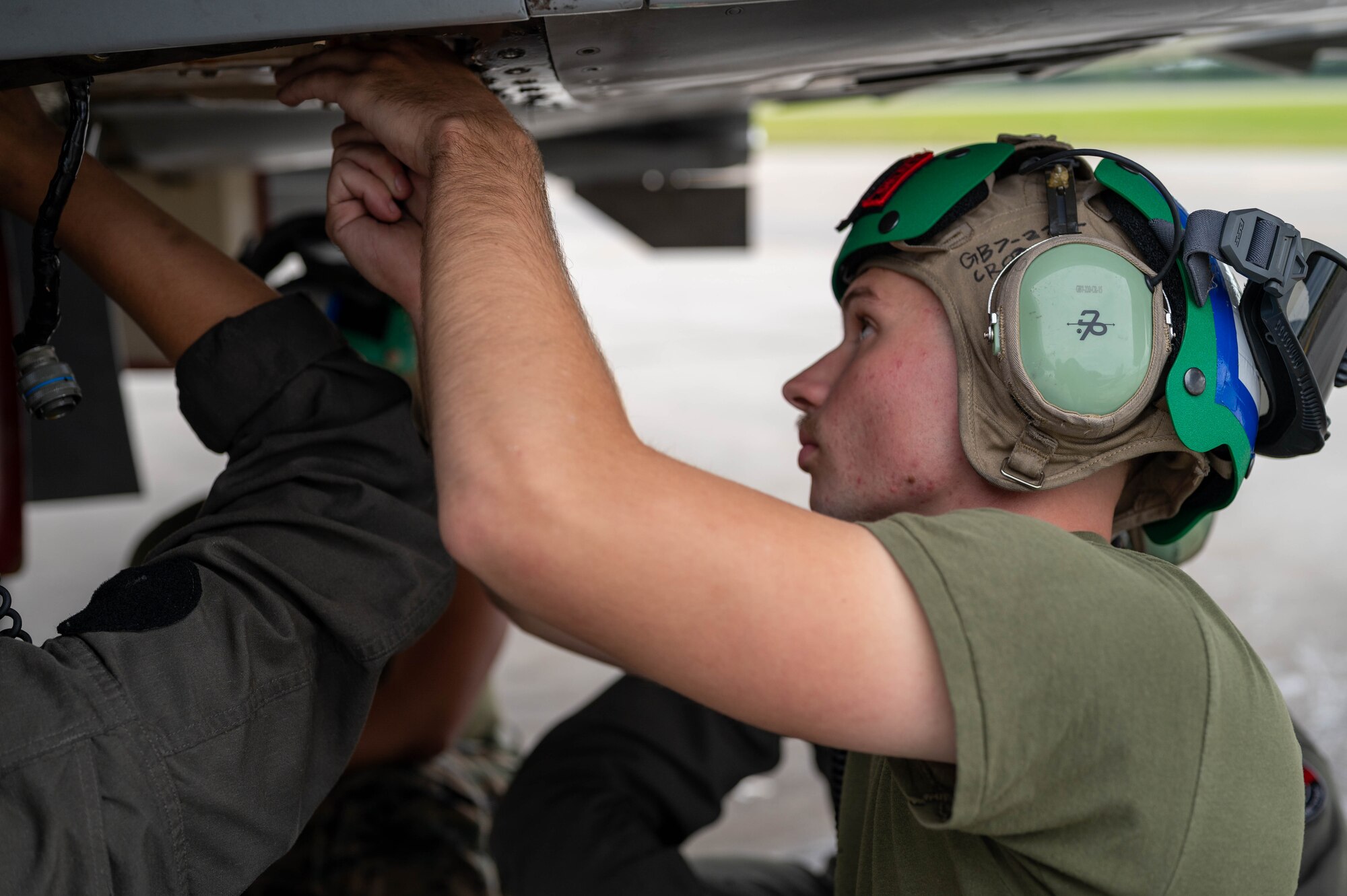 A maintainer from the U.S. Marine Corps conducts maintenance underneath an aircraft on the flightline.