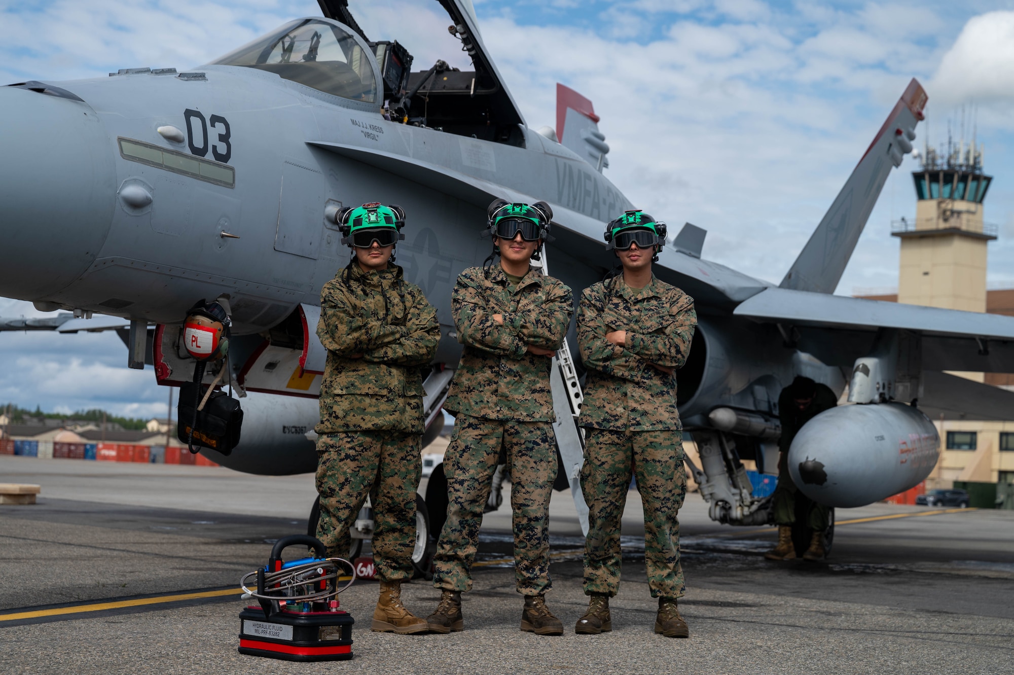 3 U.S. Marines pose in front of an F/A-18D aircraft on the flightline.