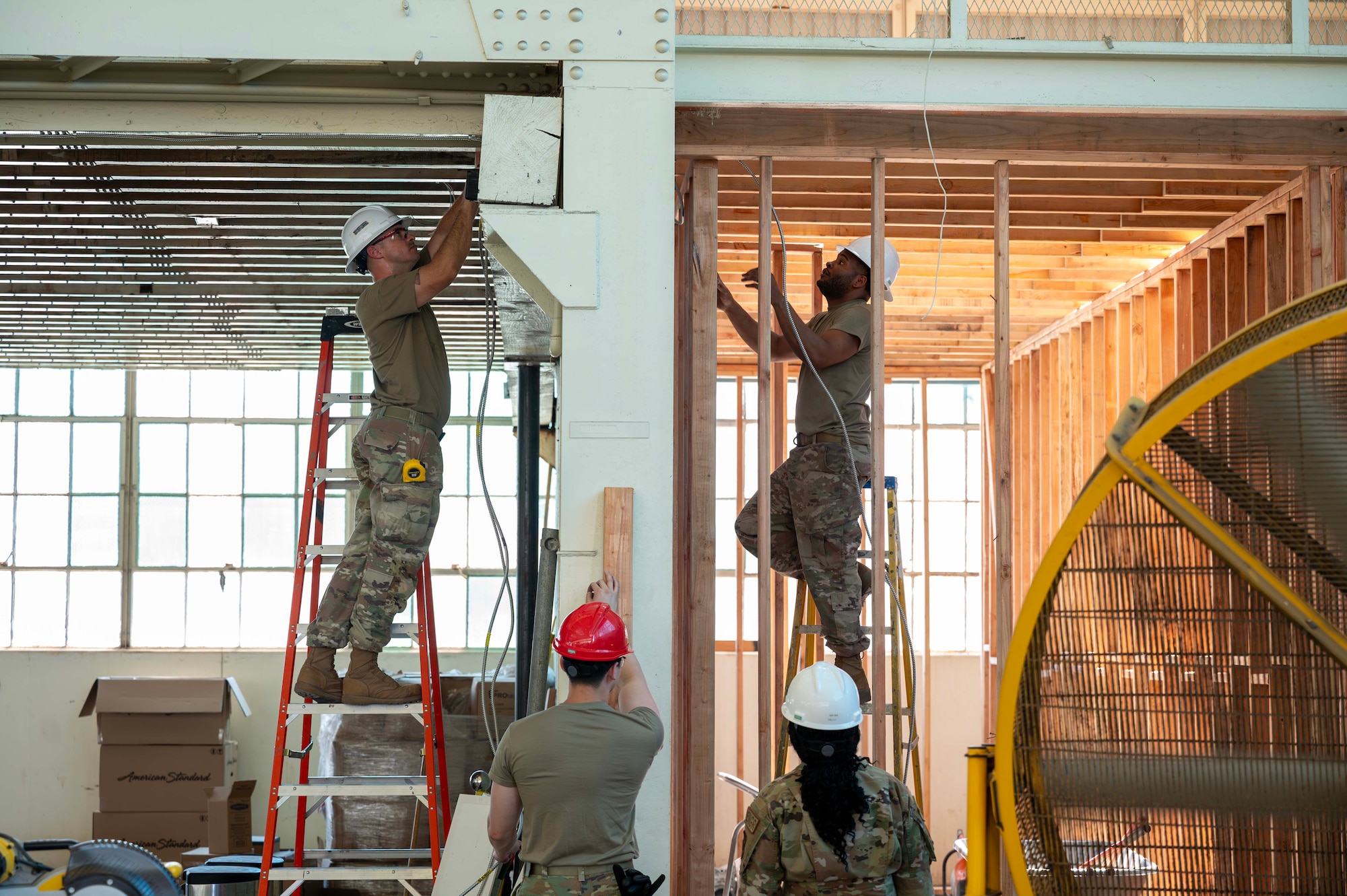 Airmen work together to install an electrical line through a wall