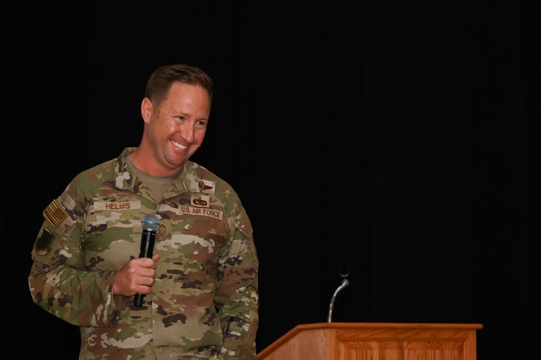 Air Force service member smiling towards audience while holding a microphone.