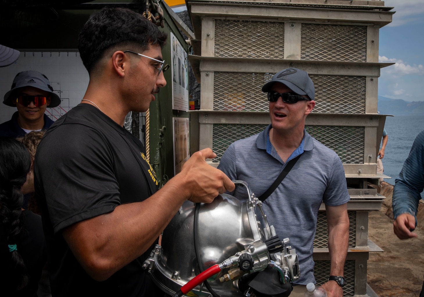 240709-N-WM182-1114 NHA TRANG, Vietnam (July 9, 2024) U.S. Army Sgt. Nicolas Jung, a deep sea diver assigned to the Defense POW/MIA Accounting Agency (DPAA), demonstrates dive equipment in front of U.S. Navy Capt. Nicholas DeLeo, commanding officer of the U.S. 7th Fleet flagship USS Blue Ridge (LCC 19) aboard a dive barge supporting the DPAA investigation of a 1971 helicopter crash site in the Bay of Nha Trang July 9. U.S. 7th Fleet is the U.S. Navy's largest forward-deployed numbered fleet, and routinely interacts and operates with allies and partners in preserving a free and open Indo-Pacific region. (U.S. Navy Photo by Mass Communication Specialist 2nd Class Caitlin Flynn)
