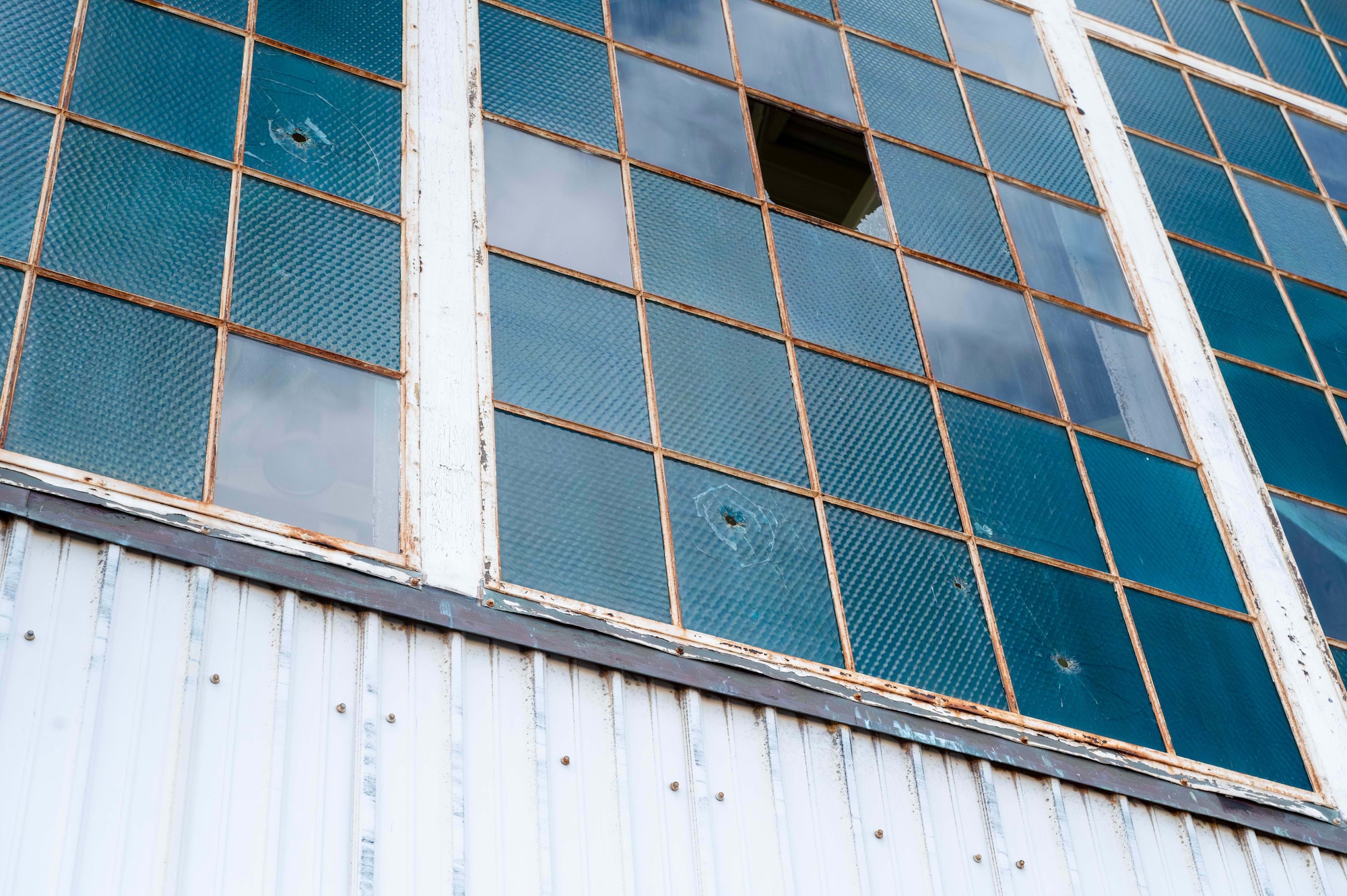 A large window pane with multiple segments can be seen with bullet holes in it. These holes are the results of attacks that took place during the attack of Pearl Harbor