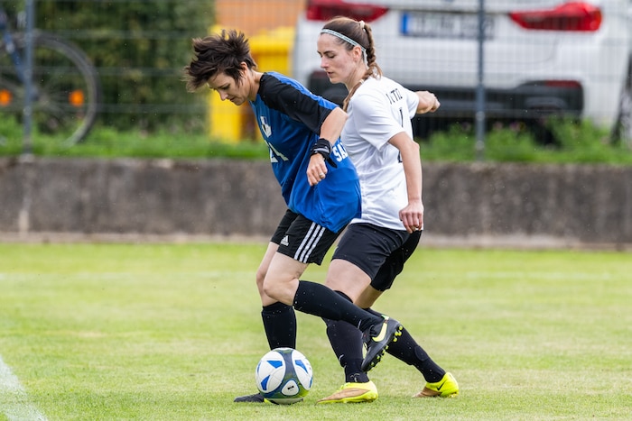 A soccer player in a blue jersey and a soccer player in a white jersey jostle for a ball.