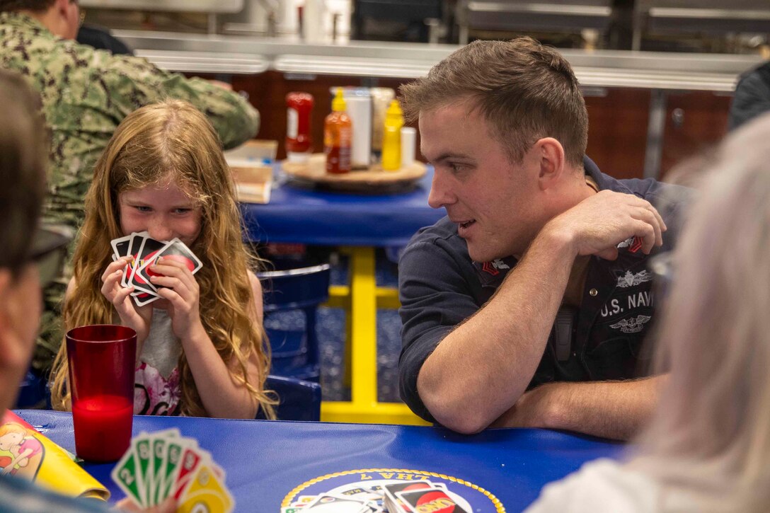 A sailor looks at a young civilian who is holding cards and smiling.