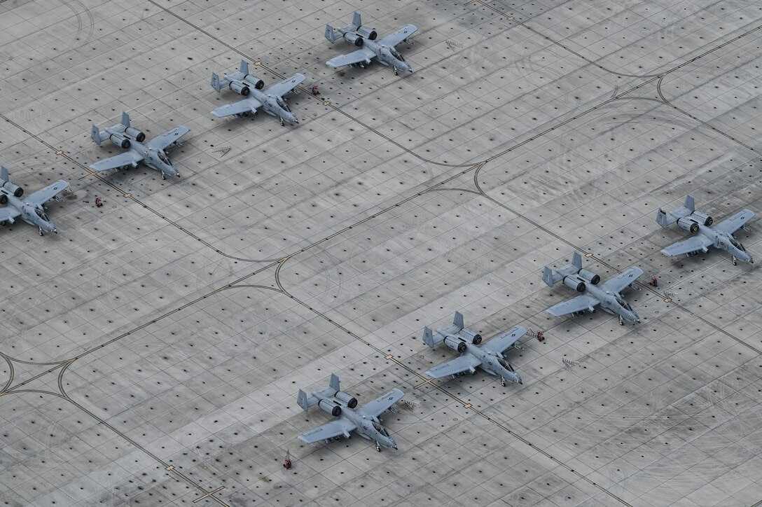 Two rows of military aircraft are parked on a tarmac during daylight.