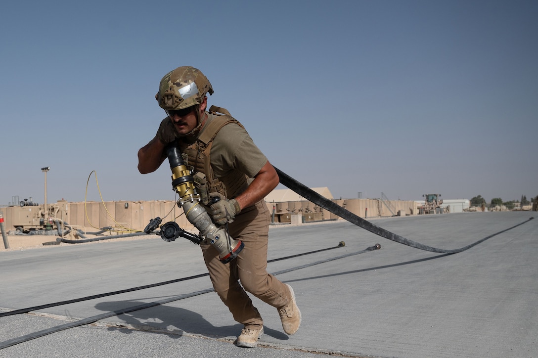 An airman wears a helmet while pulling a hose during daylight.