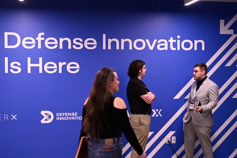 People in civilian attire gather near a sign that reads “Defense Innovation Is Here.”