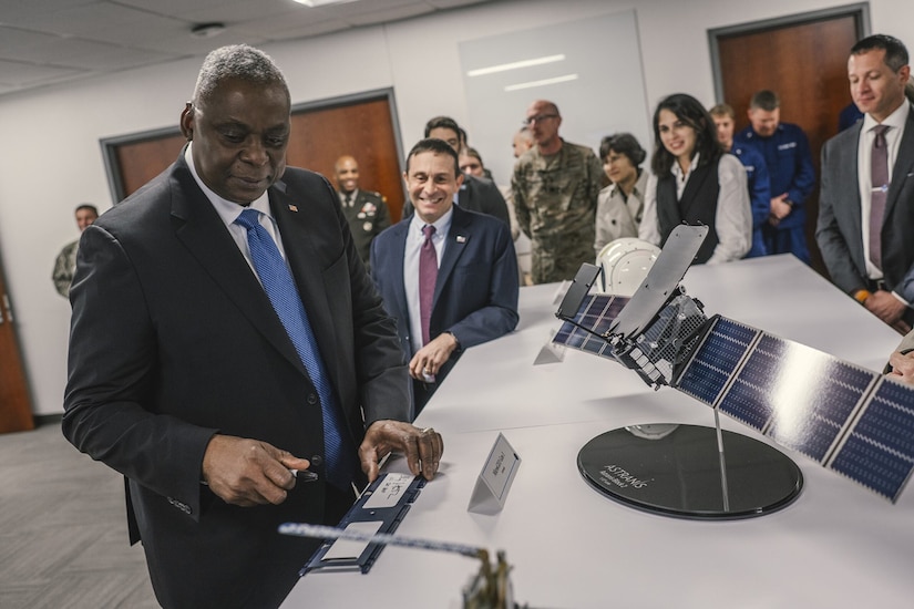 A person in a business suit stands near a technology display as people gather in the background.