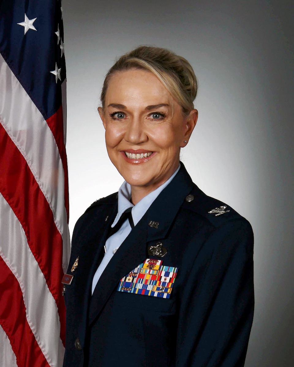 Woman in military uniform posing at camera with U.S. flag in the background