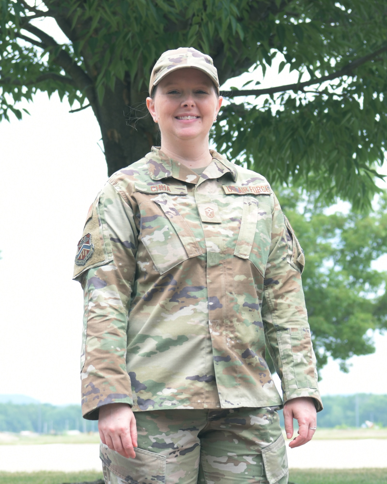 1st Sgt Heather Chua is the new Resiliency First Sergeant for the 439th Airlift Wing.  She is standing in front of a tree outside the Wing Headquarters building at Westover Air Reserve Base. She is wearing a camouflaged uniform.