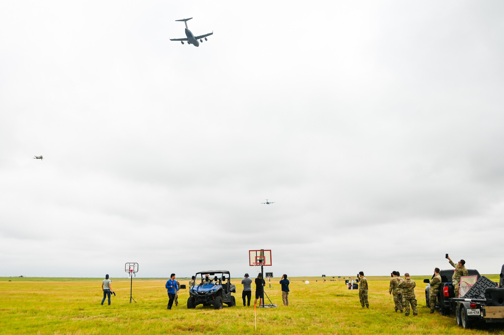 Airmen from Altus Air Force Base, Oklahoma, and a production crew from Dude Perfect watch the skies as C-17 Globemaster III aircraft fly above them at Sooner Drop Zone, Oklahoma, June 11, 2024. The 97th Air Mobility Wing hosted the Dude Perfect team for three days to help them film an episode of their show. (U.S. Air Force photos by Senior Airman Kari Degraffenreed)