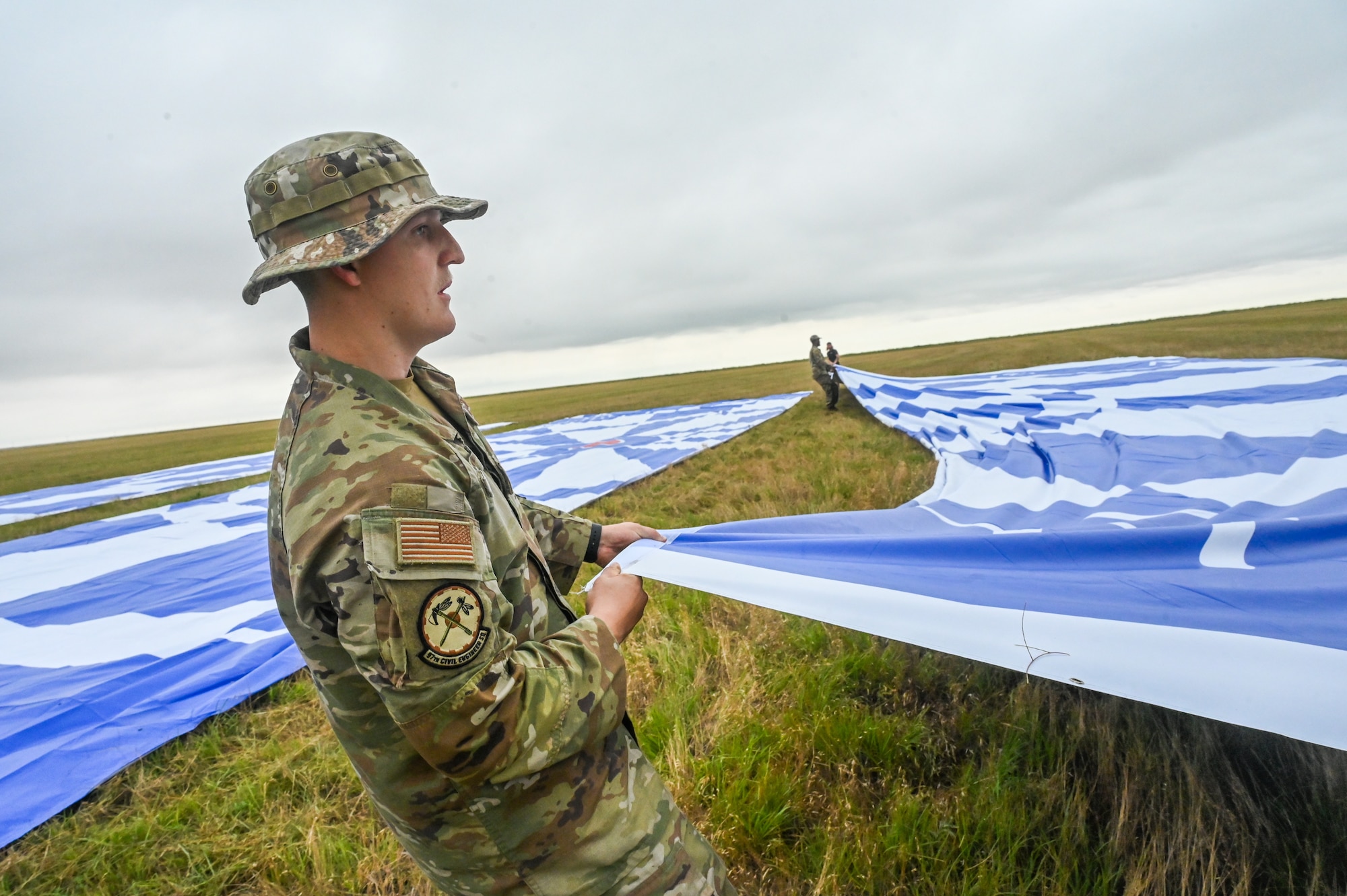 U.S. Air Force Senior Airman Jordan Sibo, 97th Civil Engineer Squadron heating and air conditioning journeyman, pulls a bullseye tarp during set up for a Dude Perfect episode at Sooner Drop Zone, Oklahoma, June 11, 2024. More than 70 Airmen from Altus Air Force Base participated in the set up and clean up of the games for the video. (U.S. Air Force photos by Senior Airman Kari Degraffenreed)