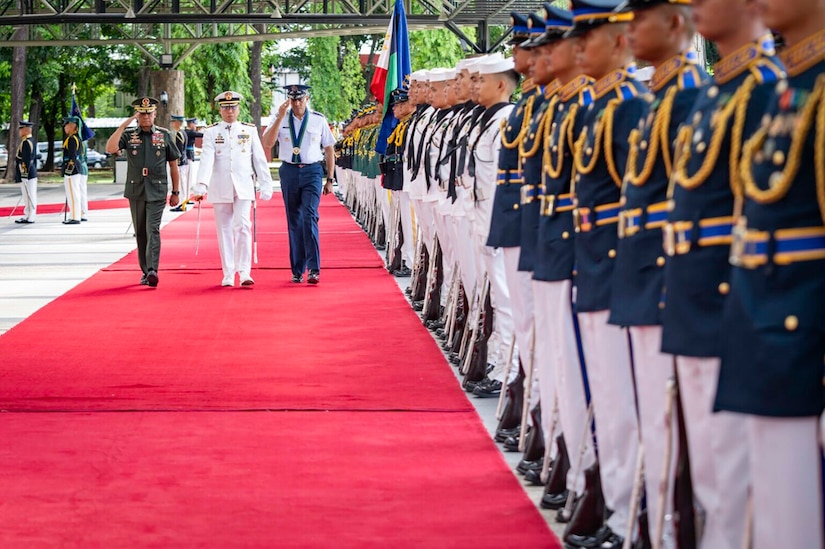 A U.S. service member in uniform salutes while walking with foreign service members as an honor cordon stands at attention.