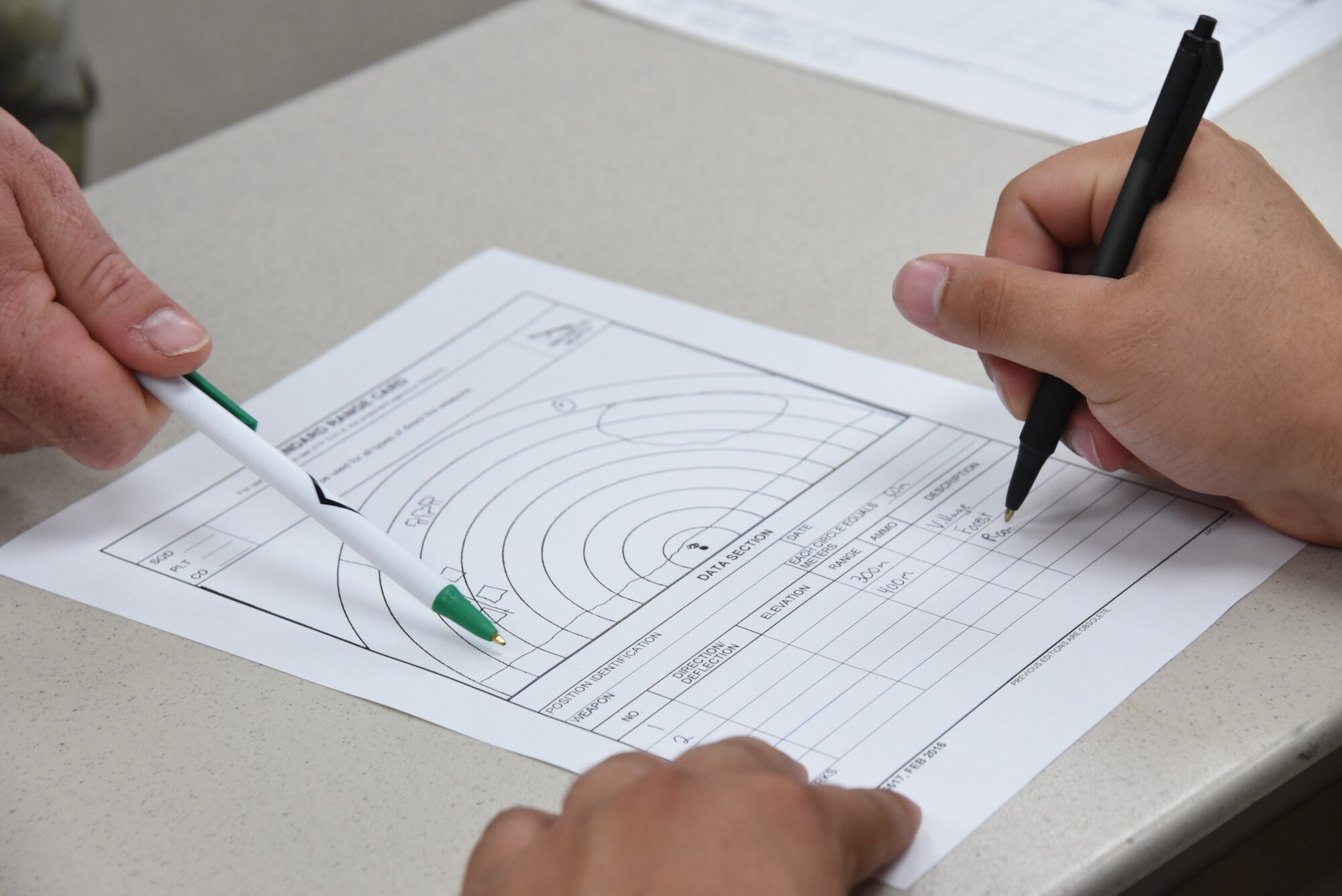 A U.S. Air National Guard Airman receives help in filling out a range card from another Airman during a class