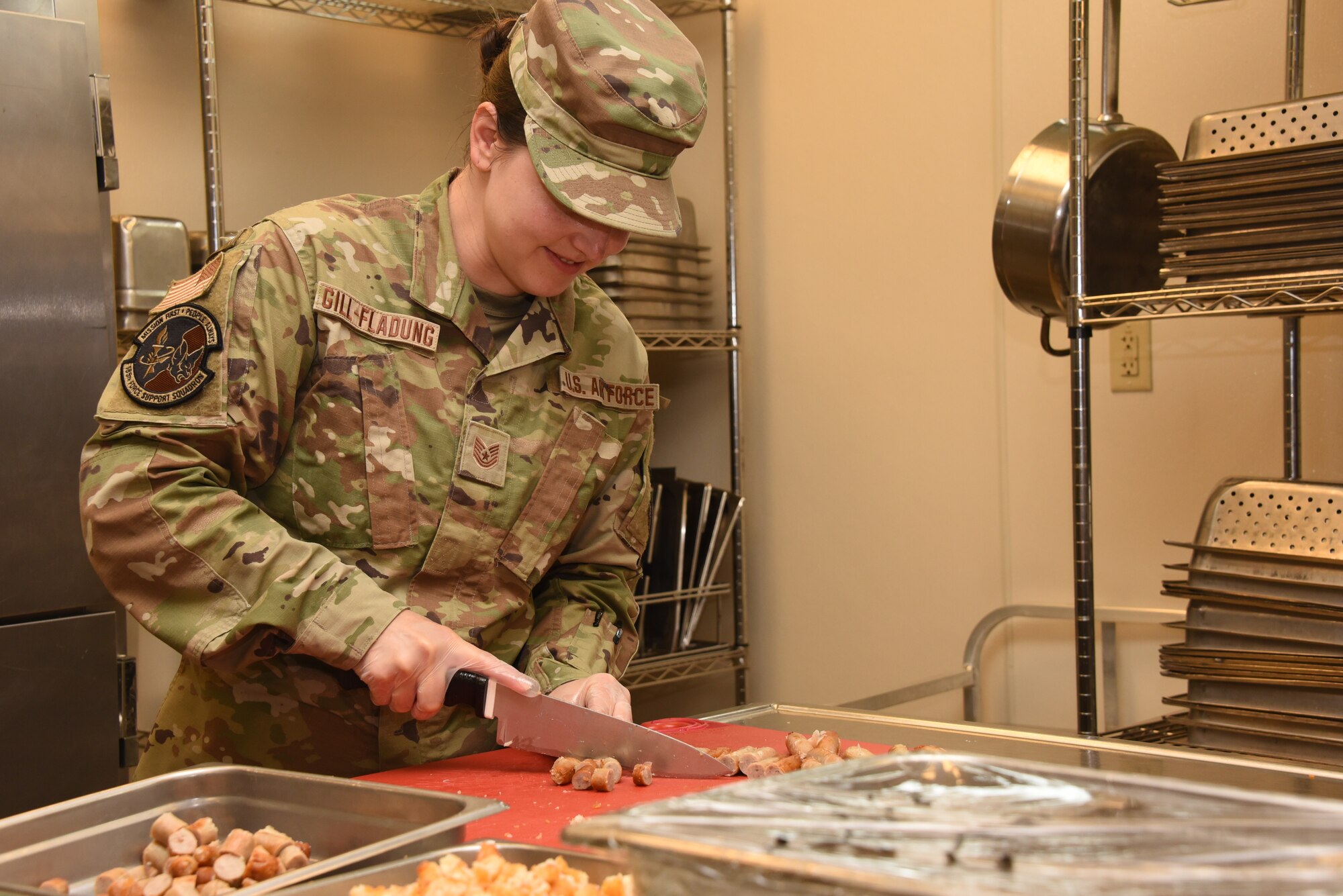 Tech. Sgt. Micah Gill-Fladung, 185th Air Refueling Wing Services Training Manager, cuts sausages