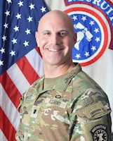 Uniformed Army Soldier smiles in front of American and USAREC flags