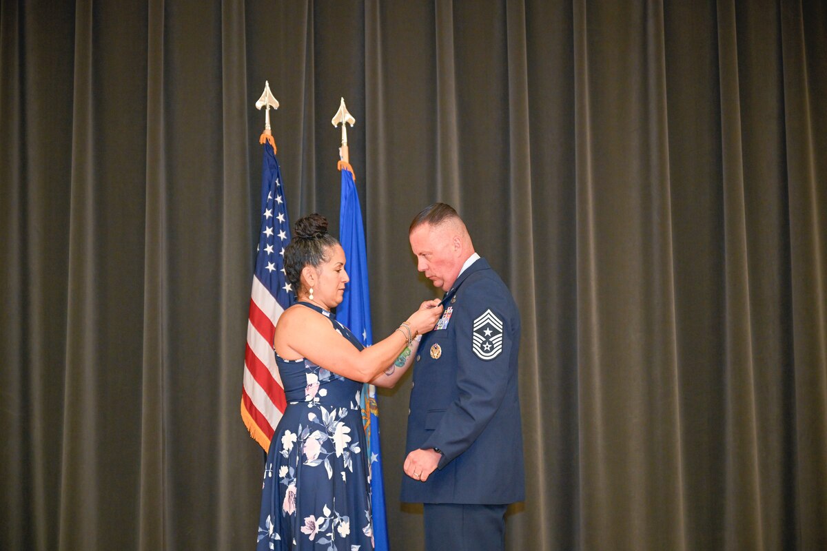 A woman pins a mans military blues uniform.