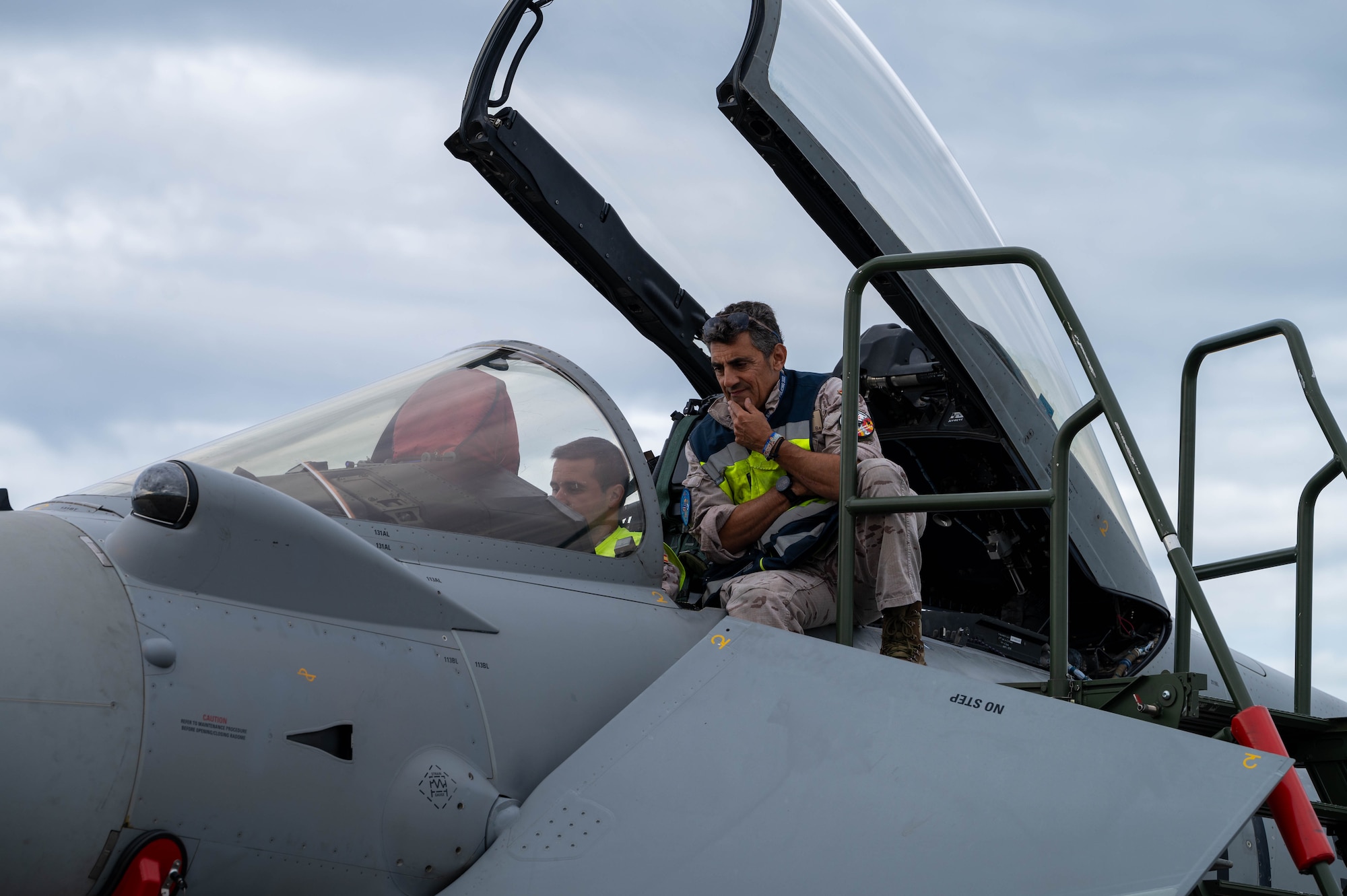 2 maintainers from the Spanish Air Force sit in the cockpit of a Eurofighter Typhoon with the canopy open to perform a routine maintenance inspection.