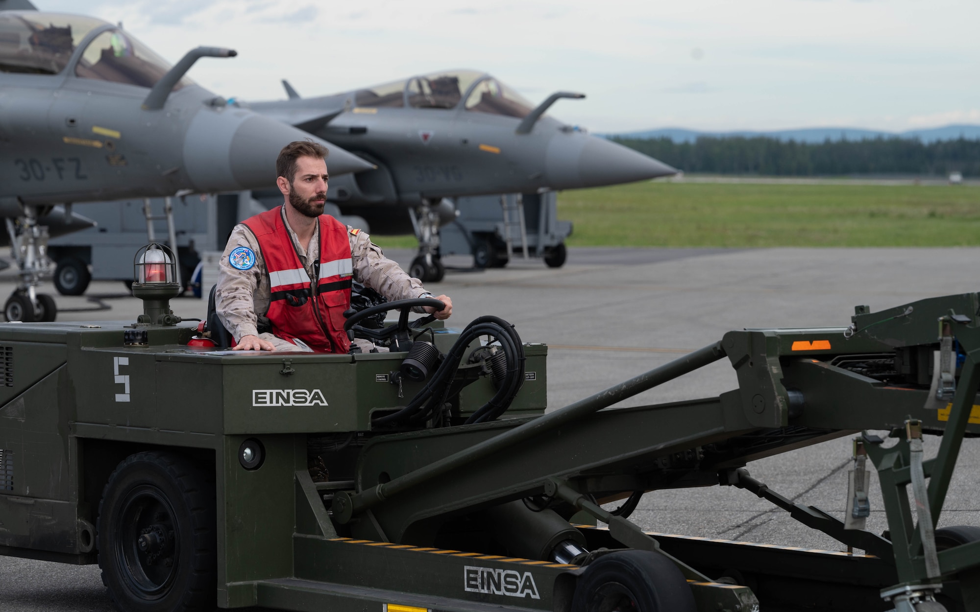 A maintainer from the Spanish Air force drives an aerial stores lift truck on the flightline with 2 Eurofighter Typhoons parked behind him.