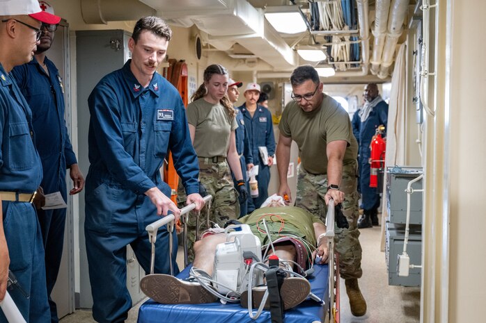 Hospital Corpsman 2nd Class Keaton Holt (left), a Tulsa, Oklahoma native, and Army Sgt. 1st Class Derek Story, a Fort Worth, Texas native, transport a patient during a medical emergency exercise aboard the San Antonio-class amphibious transport dock ship USS Somerset (LPD 25) as part of Exercise Rim of the Pacific (RIMPAC) 2024.