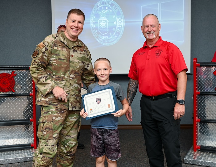 U.S. Air Force Maj. Levi Beard, 17th Civil Engineer Squadron commander, and Kevin Cotton, Goodfellow Fire Department fire chief, present Elijah, 11, with his graduation certificate during the 2024 Junior Firefighter camp at the Louis F. Garland Department of Defense Fire Academy, Goodfellow Air Force Base, Texas, July 12, 2024. After a week of different interactive lessons, the students earned the title of junior firefighters. (U.S. Air Force photo by Airman 1st Class Evelyn J. D’Errico)