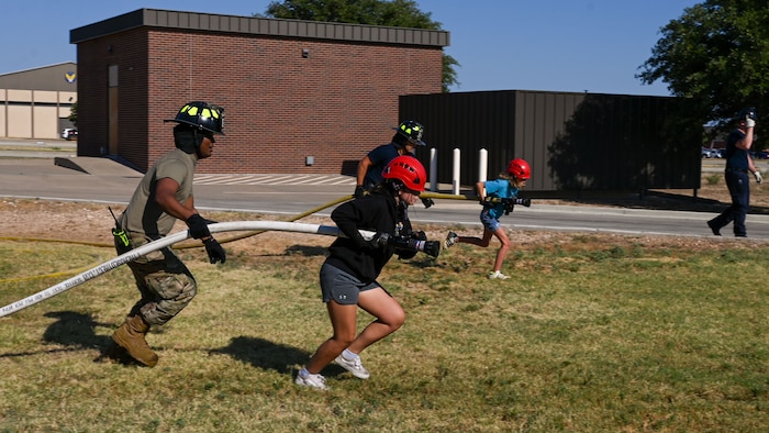 U.S. Air Force Airman First Class Wander Perez, Goodfellow Fire Department volunteer firefighter, assists Emmie in pulling the firehose to complete the Fire Hose Evolution during the fourth day of the 2024 Junior Firefighter Camp at the Goodfellow Fire Department, Goodfellow Air Force Base, Texas, July 11, 2024. Students practiced properly holding and dragging a fire hose, using its pressure to knock over a basketball and cone, and participated in a building search and rescue activity. (U.S. Air Force photo by Airman 1st Class Evelyn J. D’Errico)