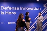People in civilian attire gather near a sign that reads “Defense Innovation Is Here.”