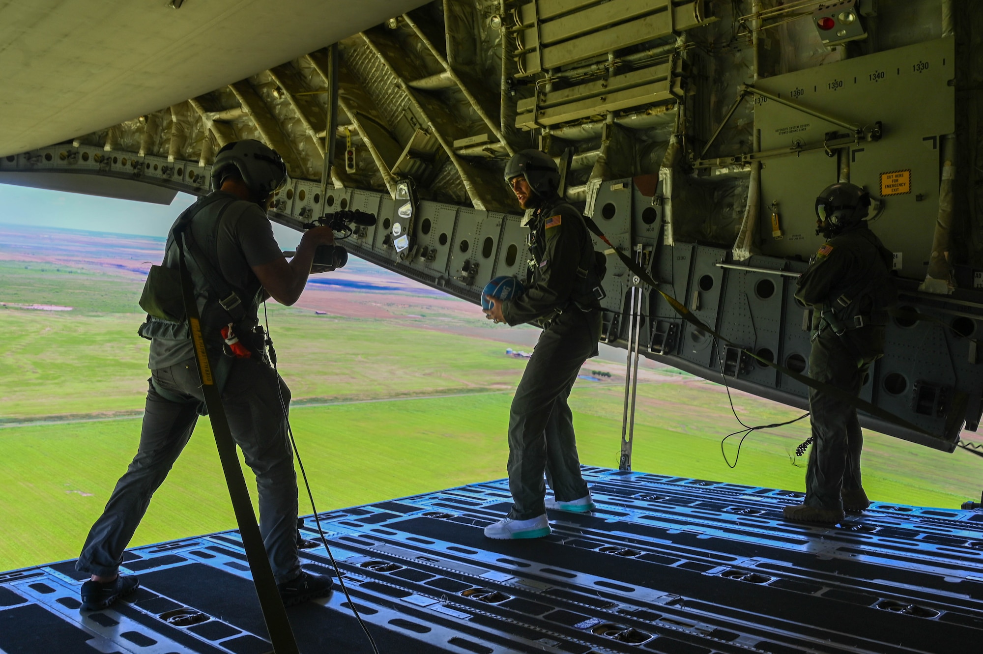 Cody Jones (center), Dude Perfect cast member, prepares to drop a basketball from a C-17 Globemaster III aircraft while U.S. Air Force Tech. Sgt. Eddie Raines (right), 58th Airlift Squadron instructor loadmaster, supervises the stunt over Sooner Drop Zone, Oklahoma, June 12, 2024. Through performing daring aerial stunts and adding a creative twist to familiar games, the Dude Perfect team and 97th Air Mobility Wing Airmen sought to create unforgettable experiences that combined the discipline of military operations with the wonder of childhood imagination. (U.S. Air Force photo by Senior Airman Trenton Jancze)