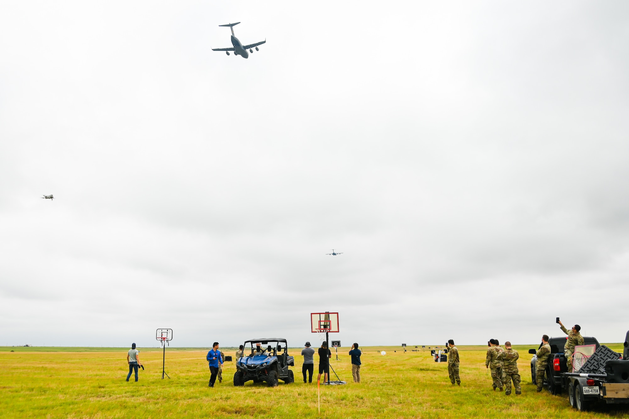 Airmen from Altus Air Force Base, Oklahoma, and a production crew from Dude Perfect watch the skies as C-17 Globemaster III aircraft fly above them at Sooner Drop Zone, Oklahoma, June 11, 2024. The 97th Air Mobility Wing hosted the Dude Perfect team for three days to help them film an episode of their show. (U.S. Air Force photos by Senior Airman Kari Degraffenreed)