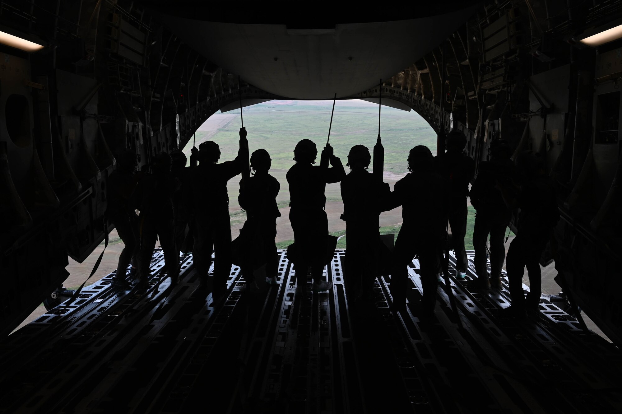U.S. Air Force instructor loadmasters from the 58th Airlift Squadron and the cast of Dude Perfect prepare to drop giant darts out of a C-17 Globemaster III aircraft at Sooner Drop Zone, Oklahoma, June 12, 2024. During the stunt, the Dudes dropped 7-foot tall darts towards an enlarged bullseye on the drop zone, while the aircraft was 300 feet above the ground. (U.S. Air Force photo by Senior Airman Trenton Jancze)