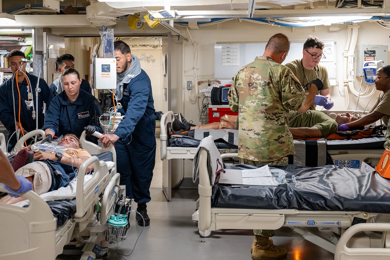 Surgeons work on two simulated patients laying on beds while in a ship.