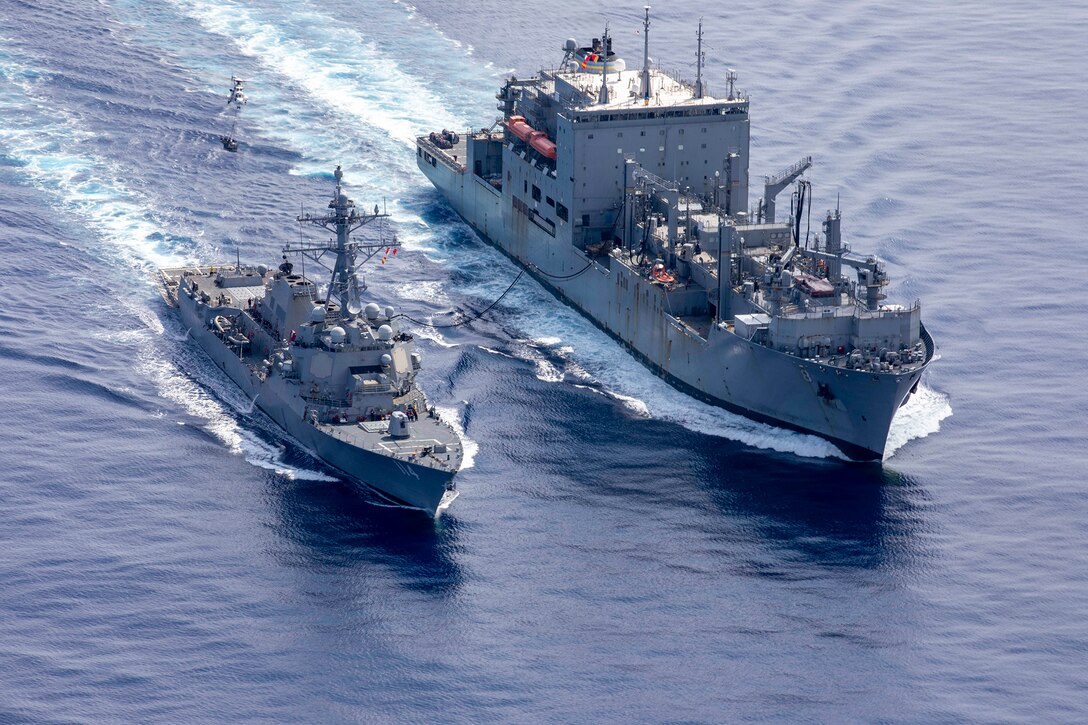 Two parallel ships are connected by a tether in open water during daylight.