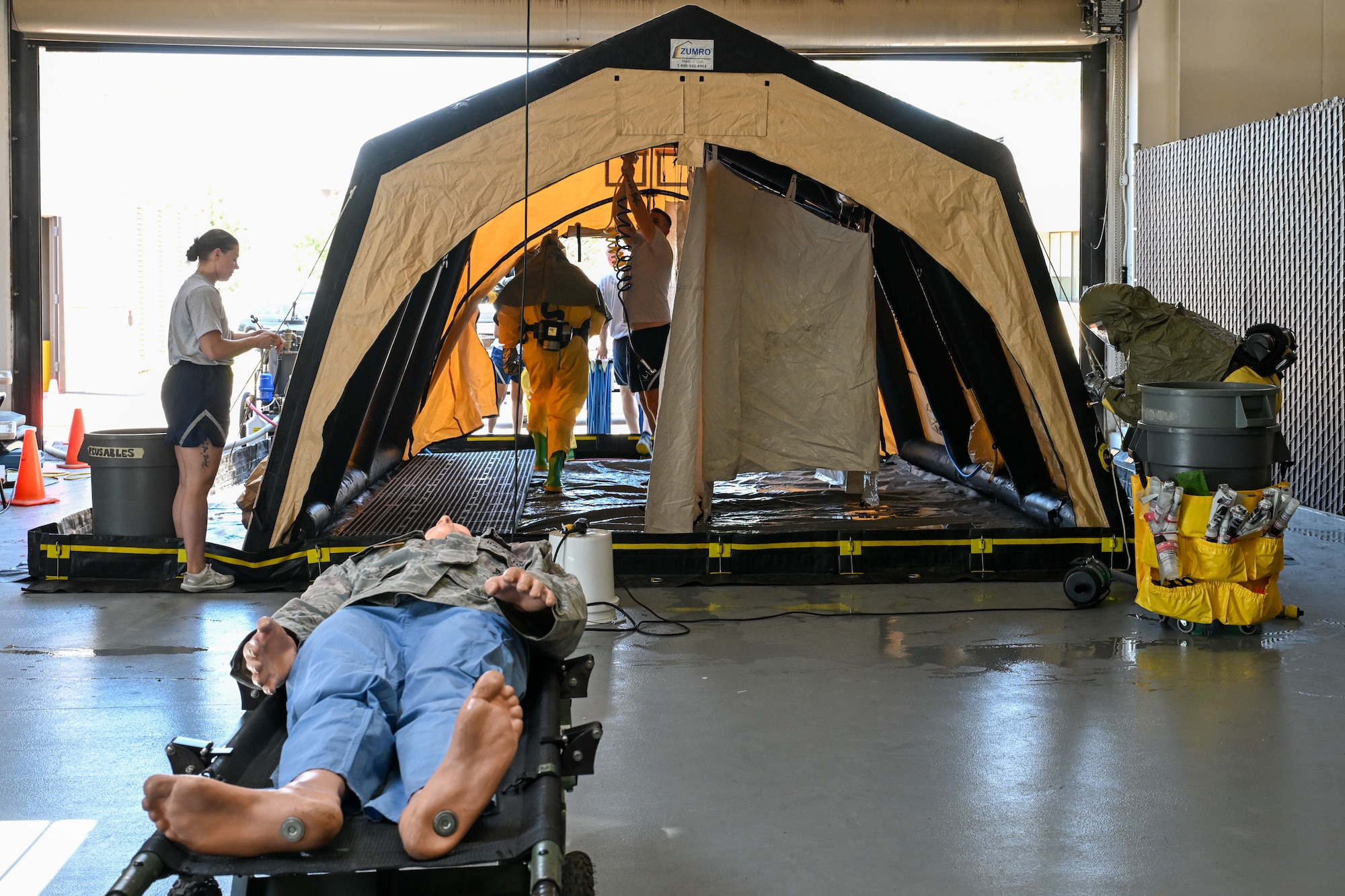A training dummy sits on a stretcher in front of the decon site
