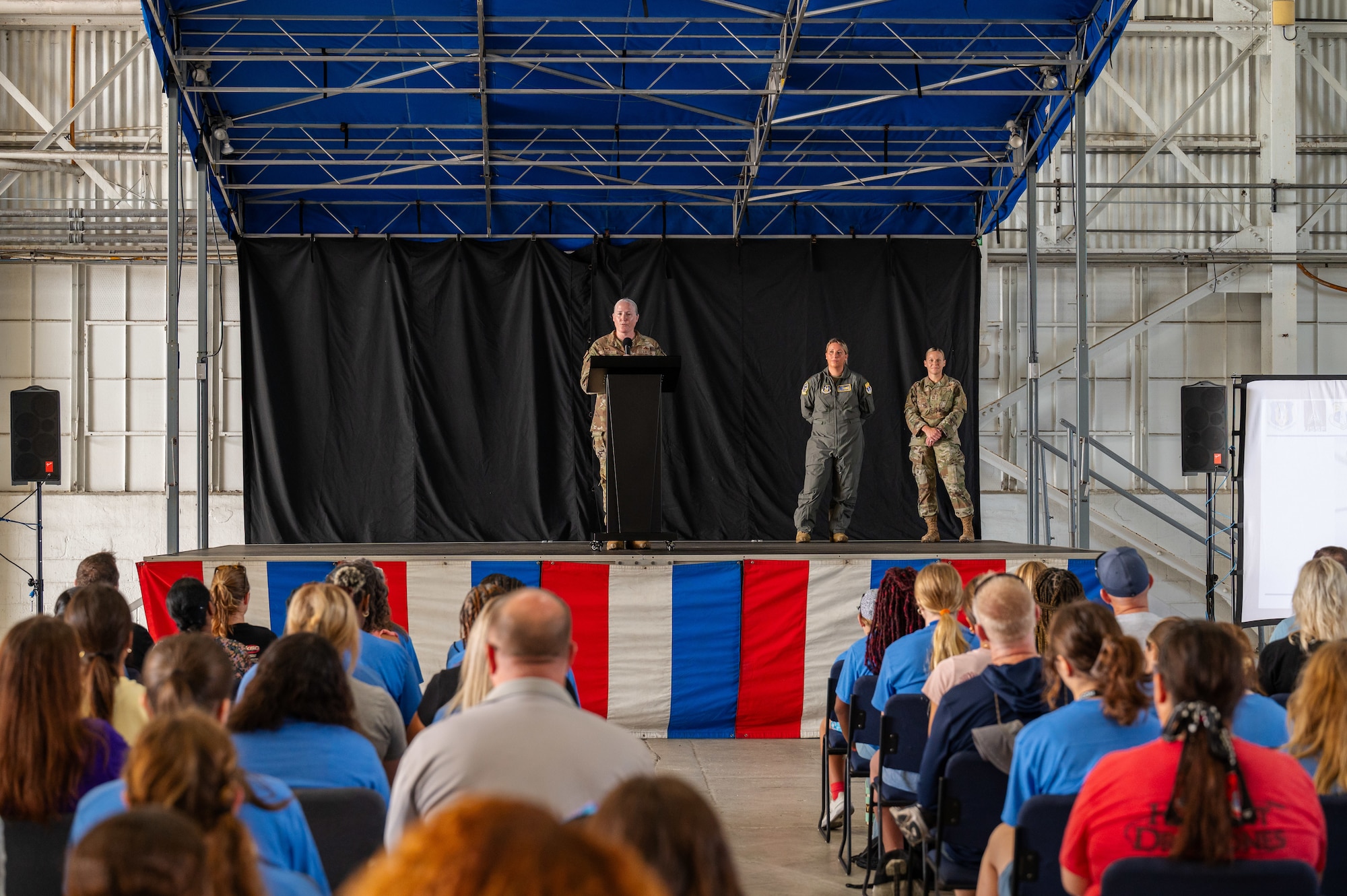 attendees sit while listening to a speaker at a lectern.