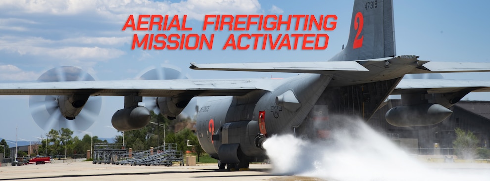 A C-130 with the engines running, water blasting out of a nozzle on the side of the aircraft with the words "AERIAL FIREFIGHTING MISSION ACTIVATED" at the top of the image.