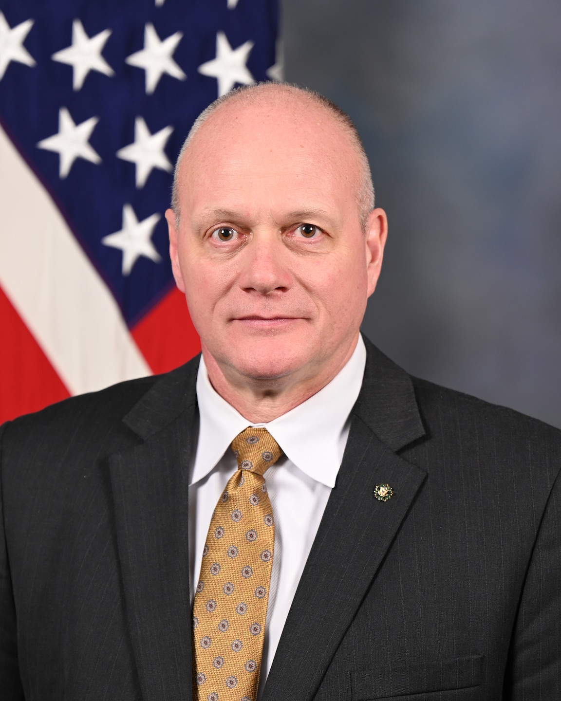 A studio shot of a man in front of an American Flag, which is behind his right shoulder.