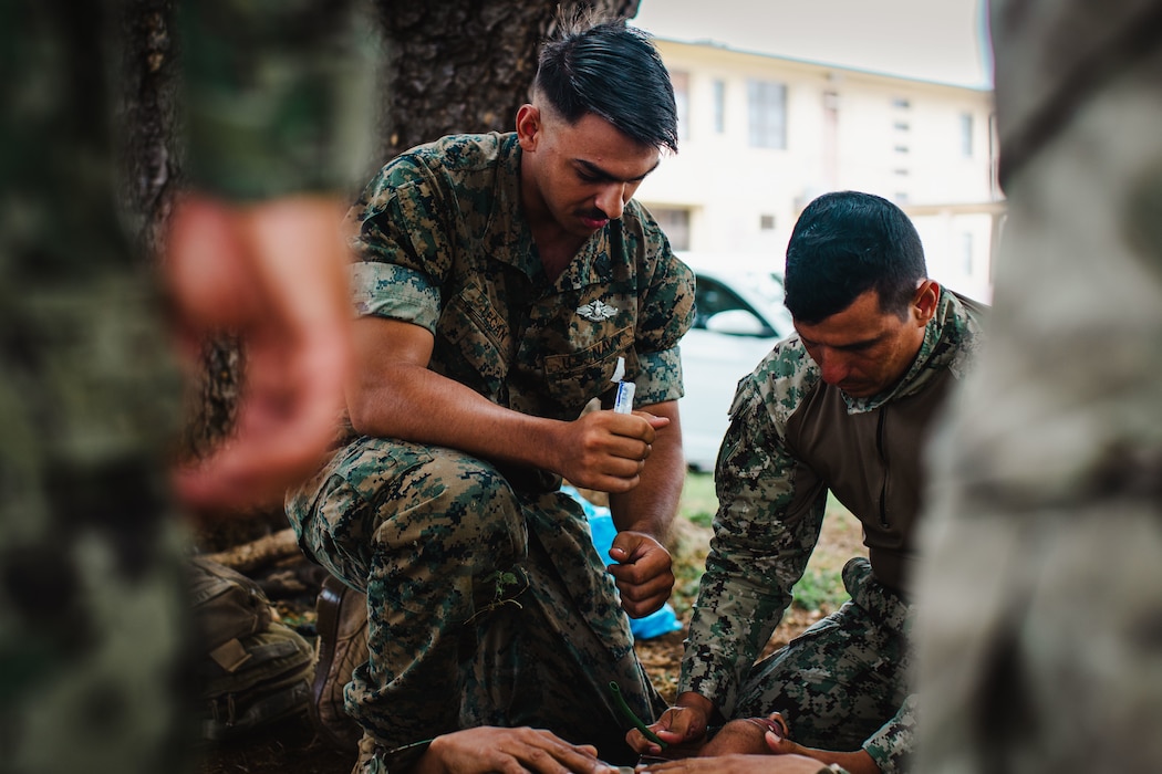 240715-M-AS577-1095 U.S. Navy Hospital Corpsman 3rd Class Garrett Legan, center, assigned to Charlie Company, Battalion Landing Team 1/5, 15th Marine Expeditionary Unit, a native of Florida, demonstrates how to clear an airway to an Ecuadorian Naval Infantry Corps marine during tactical combat casualty care practical application training at Marine Corps Base Hawaii for Exercise Rim of the Pacific (RIMPAC) 2024, July 15. Twenty-nine nations, 40 surface ships, three submarines, 14 national land forces, more than 150 aircraft and 25,000 personnel are participating in RIMPAC in and around the Hawaiian Islands, June 27 to Aug. 1. The world's largest international maritime exercise, RIMPAC provides a unique training opportunity while fostering and sustaining cooperative relationships among participants critical to ensuring the safety of sea lanes and security on the world's oceans. RIMPAC 2024 is the 29th exercise in the series that began in 1971. (U.S. Marine Corps photo by Cpl. Luis Agostini)