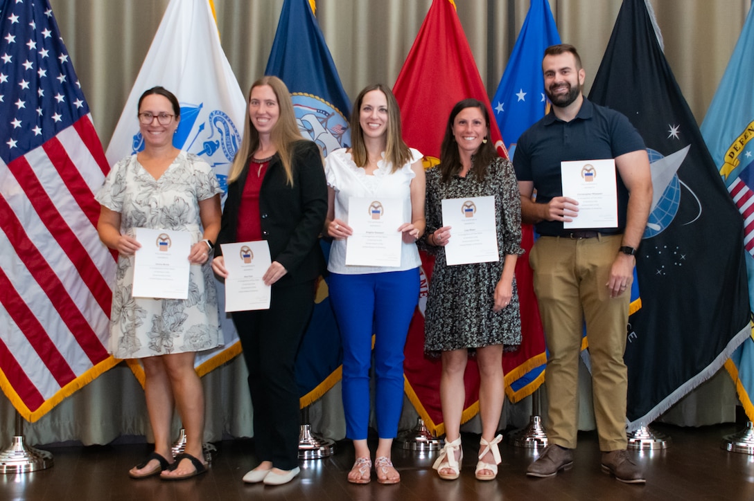 A group of people stand in front of flags holding certificates