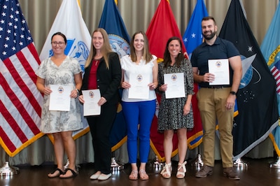 A group of people stand in front of flags holding certificates