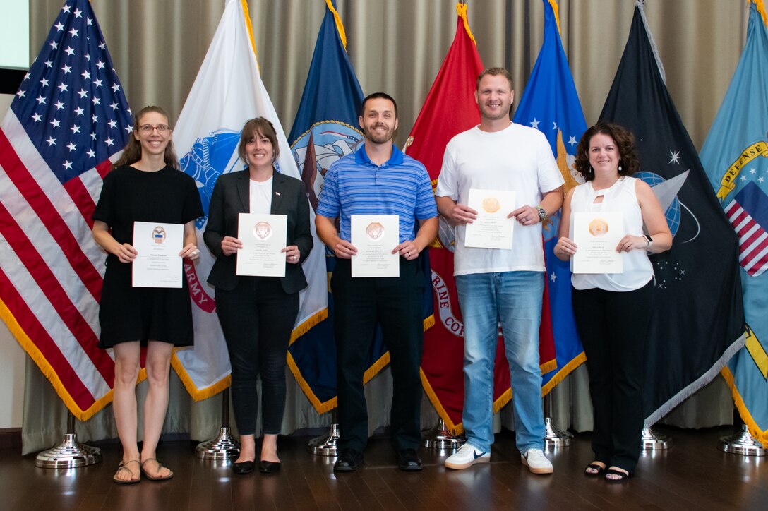 A group of people stand in front of flags holding certificates