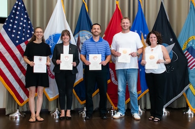 A group of people stand in front of flags holding certificates