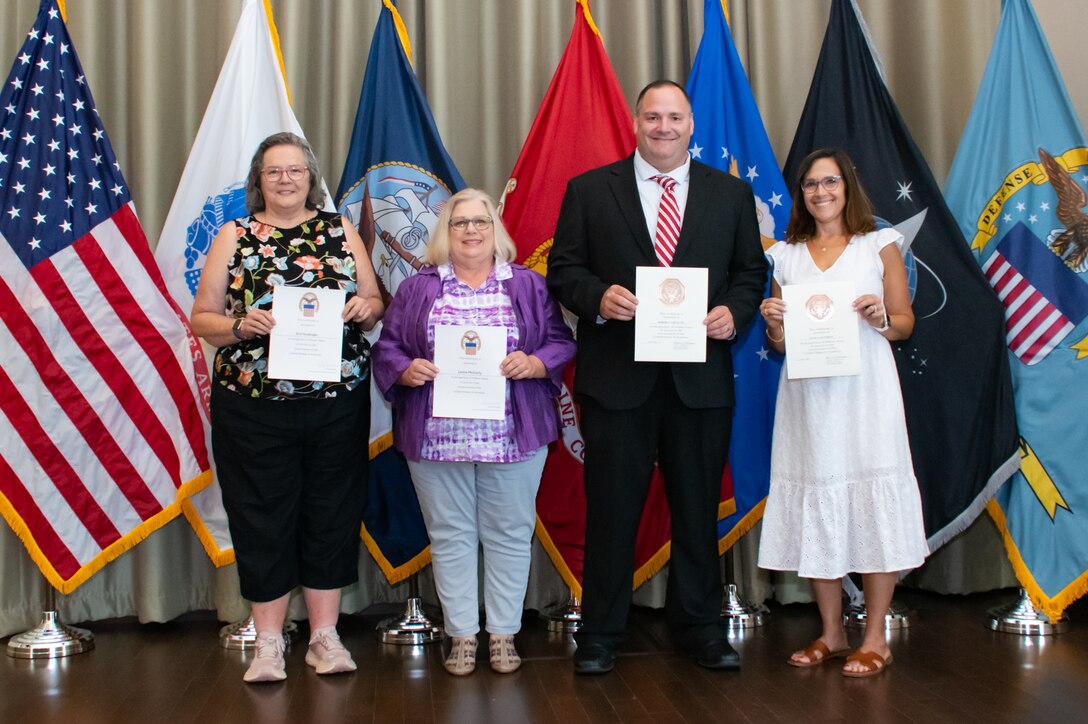 A group of people stand in front of flags holding certificates