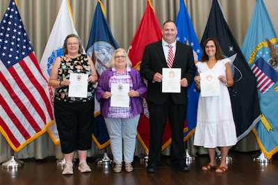 A group of people stand in front of flags holding certificates